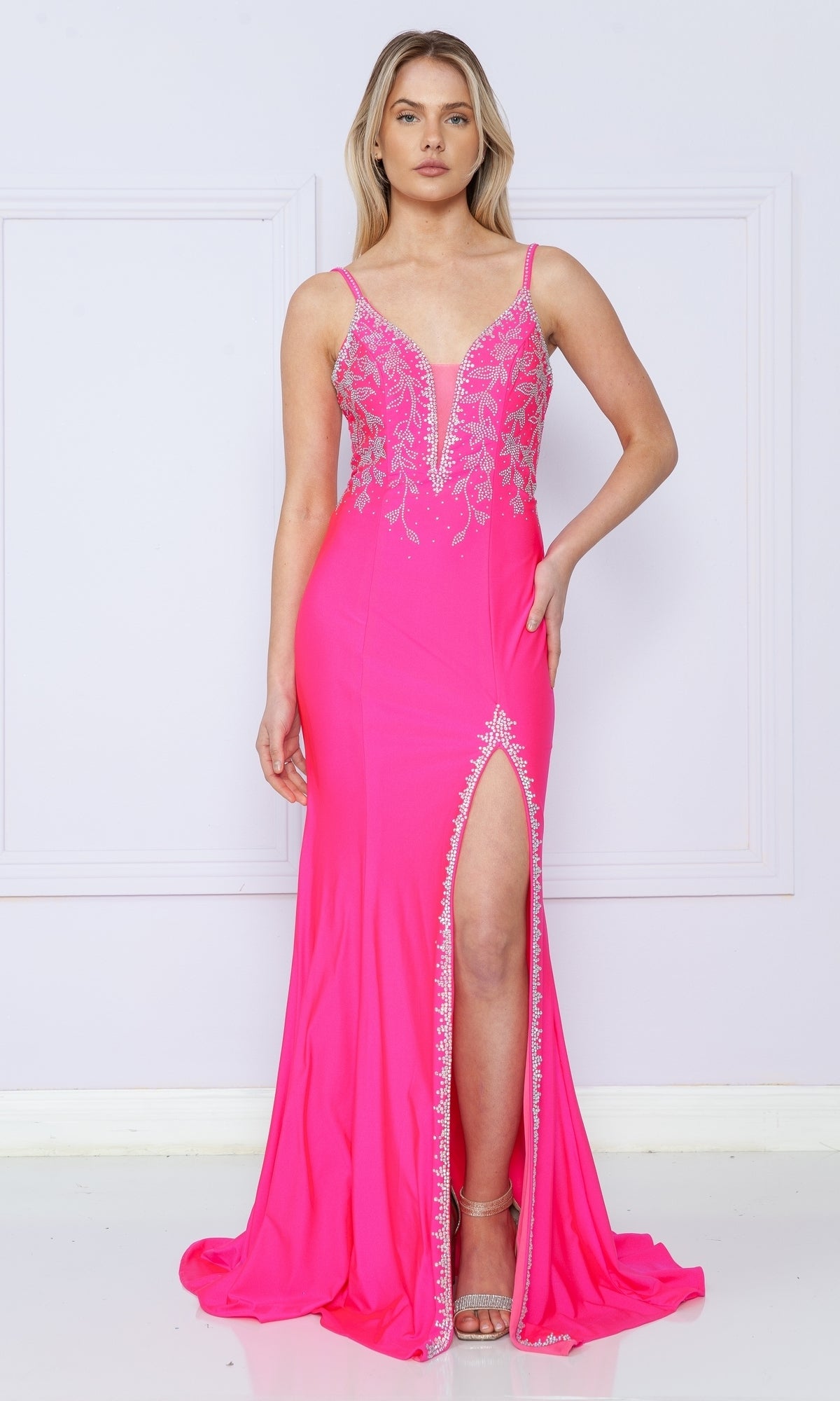 A woman wears the Backless Long Jersey Prom Dress: Poly USA 9120, a bright pink gown with silver beading, deep V neckline, and thigh-high slit, standing against a light background.